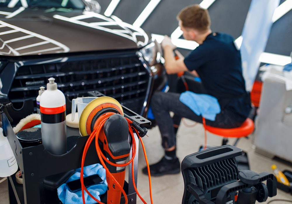 Male worker polishes headlights using polishing machine, car detailing. Preparationa before installation of coating that protects the paint of automobile from scratches. Auto tuning in workshop