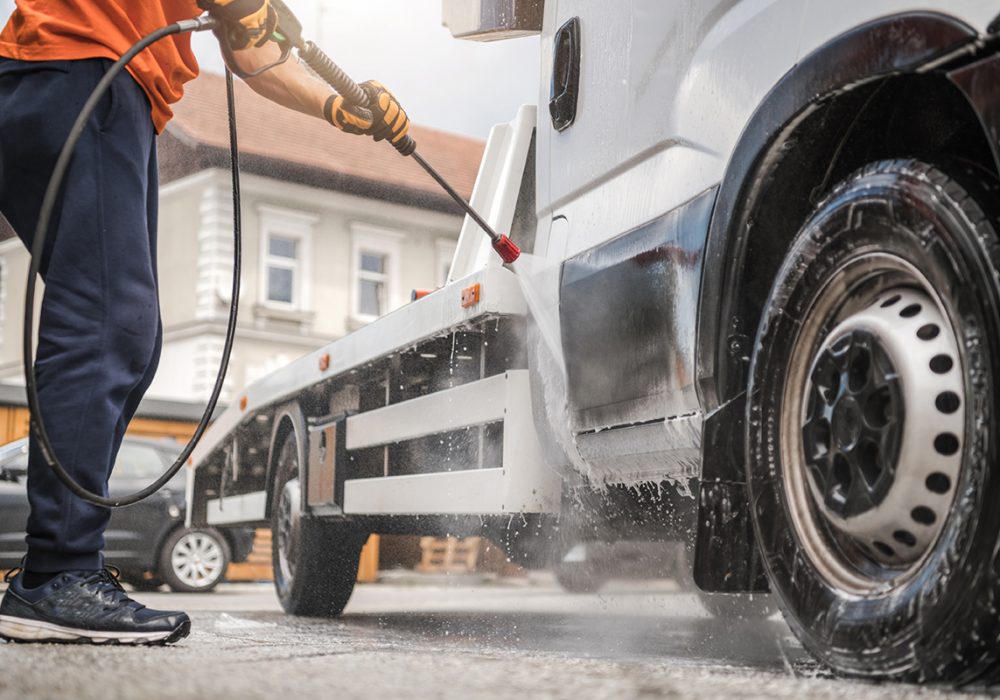 Caucasian Worker in His 40s Power Washing His Commercial Vehicle Towing Truck Inside Manual Car Wash.